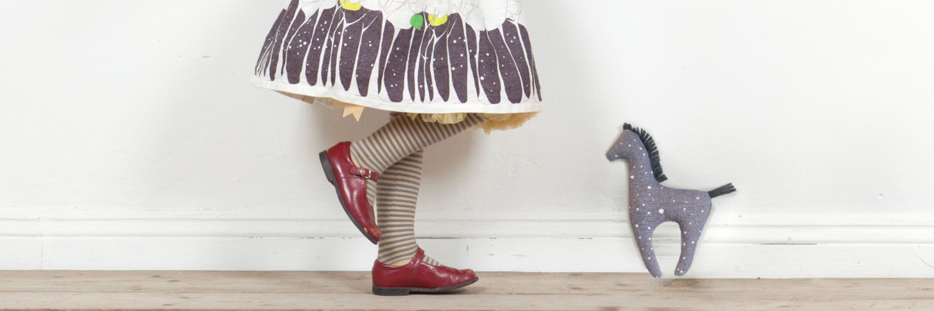 Flat lay image of childrens tights, cream with red pinstripes ,blue dots, green pinstripes and mustard squiggles. Also Navy tights with yellow and green flecks. Carefully arranged on a lime green surface with old children's books and an oak leaf or two.